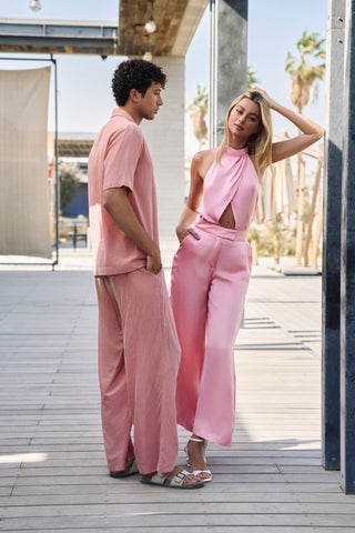 Two people in matching pink outfits standing on a wooden deck with palm trees in the background.