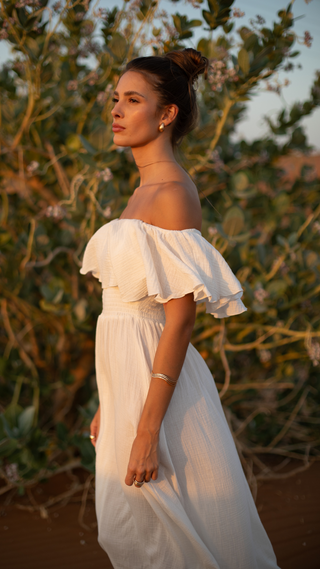 Woman in a white off-shoulder dress standing outdoors with greenery in the background